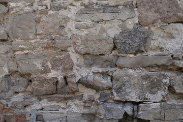 Fototapeta premium Weathered stone wall made of irregular rocks and mortar. Natural architectural texture with historic character and construction details.