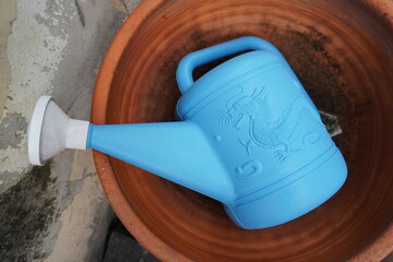 Bright blue watering can with dragon motif rests inside a terracotta pot © Thanakrit