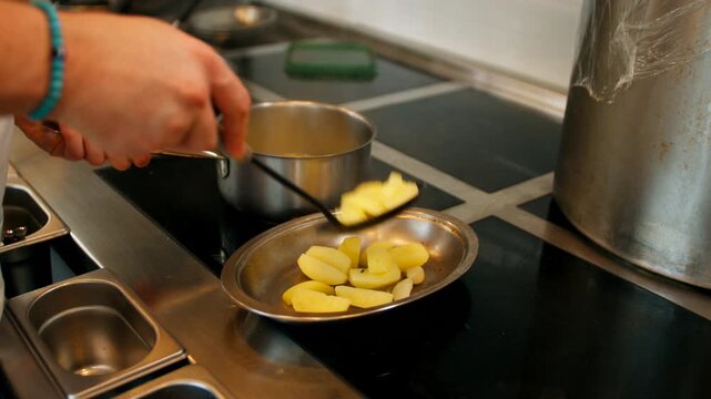 Medium shot of a chef cooking in a commercial restaurant kitchen, boiling sauce in a stainless steel saucepan next to a pan with potatoes on an induction stove