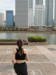 Fototapeta premium Rear view of young woman jogging towards city skyline in urban park