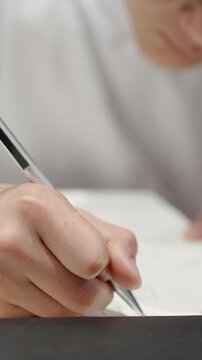 Close-up of student hand writing in notebook with soft blurred background. Vertical shot of education detail, homework, planning, school notes and focused learning concept.