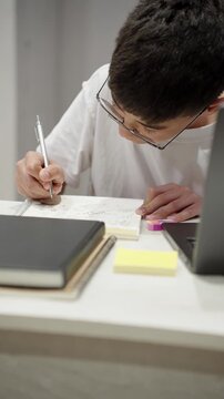 Vertical shot of teenage student writing notes in notebook at home desk. Focused homework, school preparation, study routine and education lifestyle concept.