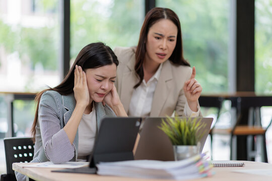 Businesswoman experiencing deep emotional distress and discomfort, covering ears to block out a critical colleague pointing a finger and creating a hostile work environment