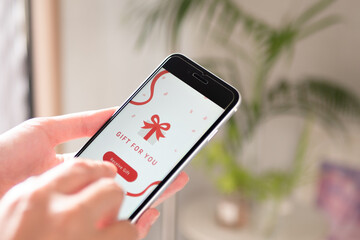スマホに届いたソーシャルギフト（eギフト）を受け取る女性の手元。画面はオリジナル制作 © Keyglad