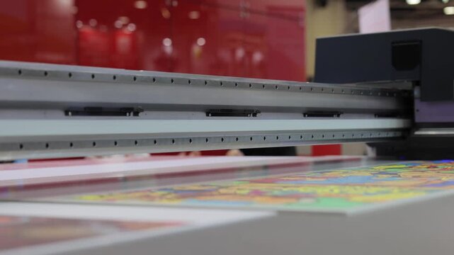 Industrial uv printer head moving back and forth to print colorful graphic design on flat material surface in professional print shop.