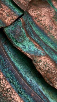 Macro closeup of textured copper roofing sample showcasing vivid green and teal oxidation patterns softly lit with diffused side lighting against a muted neutral background.