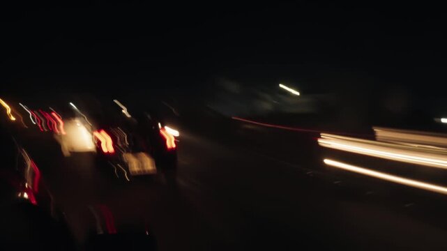 Abstract and blurry point of view shot from inside a vehicle driving fast on a dark highway, with colorful light trails from other cars creating a sense of speed and motion