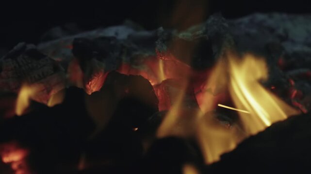 Intense close-up shot of red hot charcoal embers burning with bright orange flames, creating a warm and mesmerizing fiery background perfect for concepts of heat, energy, and comfort