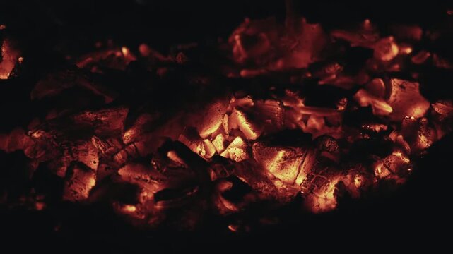 Intense red hot coals glowing inside a barbecue grill or fireplace, radiating heat and creating a warm, cozy atmosphere. The smoldering embers create a dynamic, fiery background