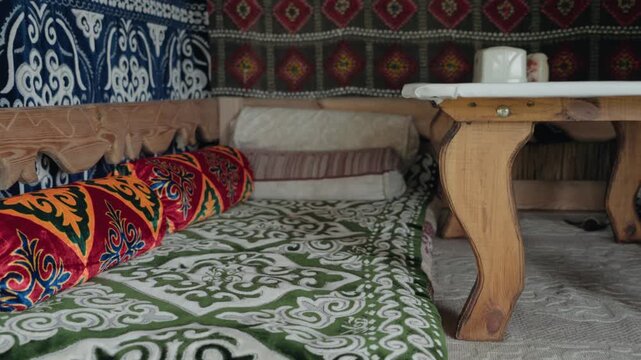 Colorful interior of a traditional Central Asian yurt, featuring ornate textiles, patterned cushions, and a low wooden table, showcasing a nomadic and ethnic lifestyle and cultural heritage