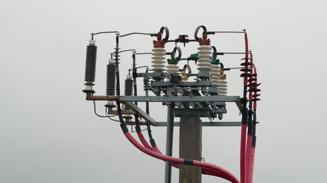 High voltage electrical tower with insulators, wires, and transformers against a grey sky, showcasing the complexity of power distribution infrastructure and electrical engineering components