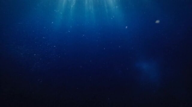 Sun rays penetrating deep blue water with bubbles.