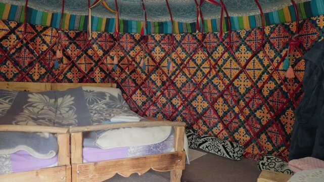 Authentic interior of a traditional mongolian yurt featuring colorful ornamental walls, a wooden bed, and various household items, showcasing the unique nomadic lifestyle and cultural heritage