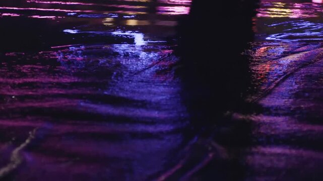 Colorful city lights reflecting and rippling on the wet asphalt surface of a street at night after a rain shower, creating an abstract and moody urban atmosphere with a cinematic vibe