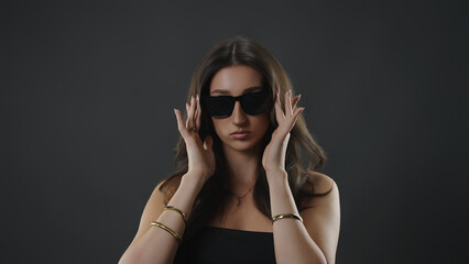 Naklejka premium Young woman styling her dark sunglasses, projecting elegance, confidence, and modern fashion