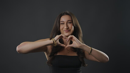 Fototapeta premium Young woman smiling at camera, making a heart shape with her hands