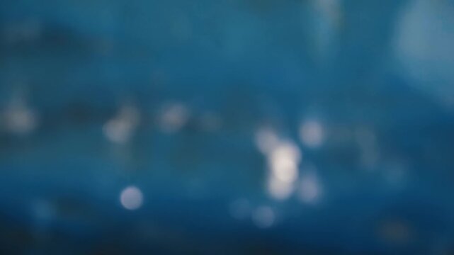 Defocused sunlight glittering and reflecting on a flowing blue water surface creating a tranquil and relaxing abstract background with sparkling bokeh lights for a calm summer scene