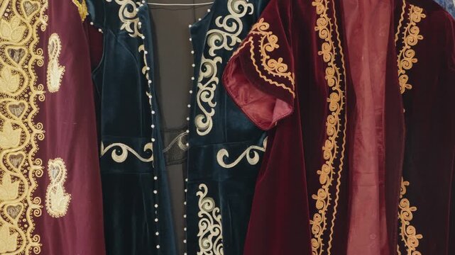 Colorful traditional kazakh clothing made of velvet and silk with intricate golden embroidery hanging on display. Authentic national costumes representing the rich cultural heritage and craftsmanship