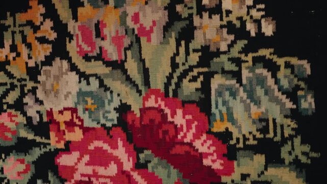 Close-up of traditional handwoven rug with intricate floral rose motifs and pixel-like tapestry texture on a dark vintage background, showing detailed woven craftsmanship and ornamentation