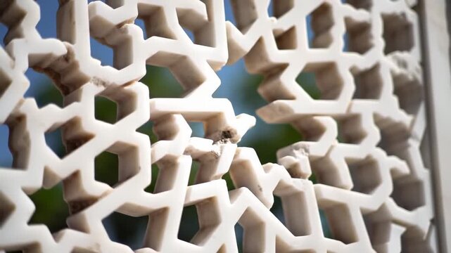 intricate white marble geometric lattice screen with blurred green foliage and blue sky background, architectural detail, detailed pattern, ornamental cutout
