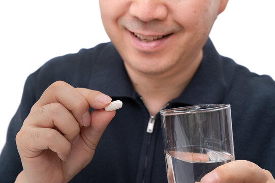 약을 복용하기 전 손가락으로 흰색 의료용 알약을 들고 미소 짓는 남성의 클로즈업.