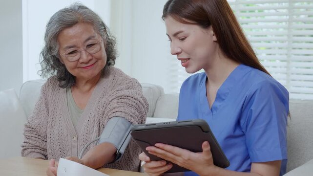 Asian woman nurse measuring blood pressure senior patient, medical checking for hypertension monitoring with digital tablet, caregiver support elderly woman with arterial blood pressure device.