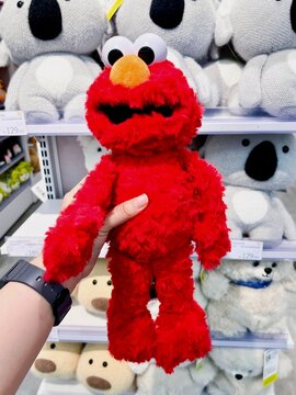 Jakarta, Indonesia - June 15th, 2026 - Hand holding red elmo doll isolated on vertical indoor store shelf background.