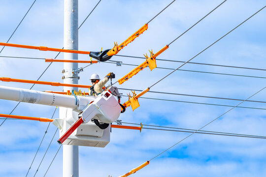 Utility lineman in bucket truck installing bright orange line guards and insulated blankets on high voltage overhead power lines