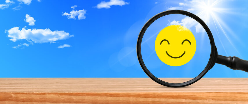 Yellow smiling face highlighted by magnifying glass under blue sky perfect for finding positive life energy and happy feedback
