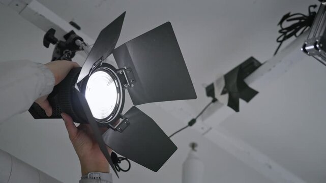 Low Angle Close up of Gaffer Hands Adjusting Professional Fresnel Studio Light with Barn Doors