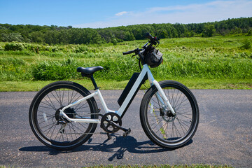 Fototapeta premium E-bike white step-through commuter electric bike sitting on a paved bicycle trail on a perfect summer day