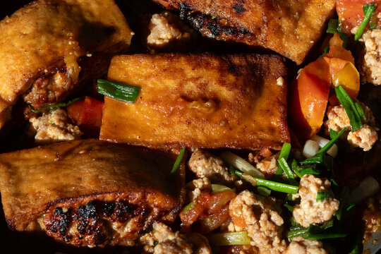 Close up of delicious braised stuffed tofu with minced meat and tomato sauce, garnished with scallions in a pan.