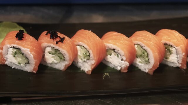 Sushi preparing. Garnishing food. Gloved chef hand tweezers adding black caviar on philadelphia rolls row with wasabi salmon portion on plate.