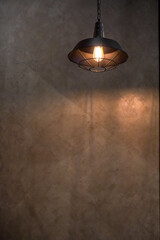Industrial pendant light with exposed bulb illuminates textured concrete wall © Thanakrit