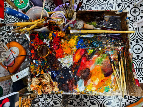 Vibrant messy artist palette covered in glossy paint, scattered brushes and tubes, dried paint