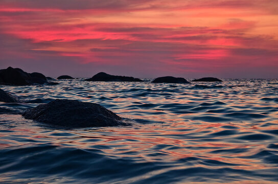Vibrant sunset over rocky coastal waves, pink and coral sky reflecting on rippling ocean surface.