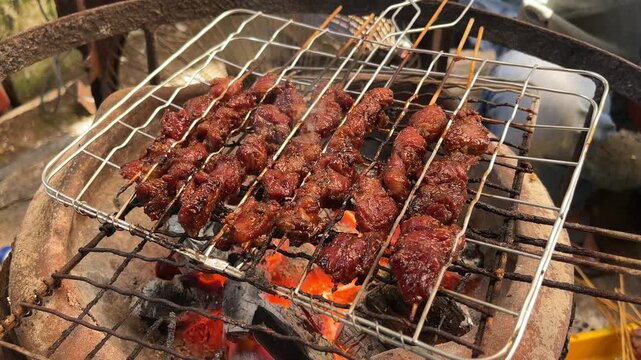 close up view of goat or beef satay grilled over a fire and charcoal. grilling tool. eid al adha, idul adha. sate kambing, sapi. indonesian food or culinary. 