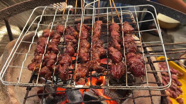 close up view of goat or beef satay grilled over a fire and charcoal. grilling tool. eid al adha, idul adha. sate kambing, sapi. indonesian food or culinary.  front