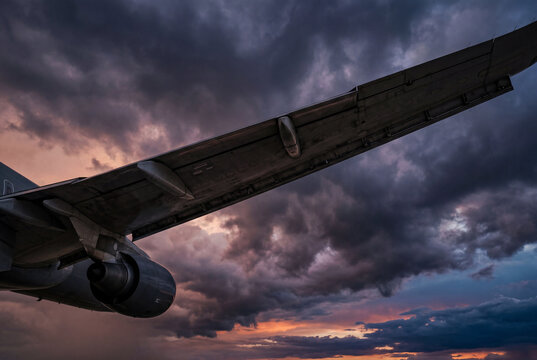 Underside of a large commercial airplane wing flying through a dark stormy sky at dusk