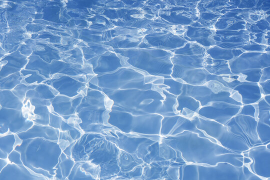 Blue swimming pool water background with bright caustic light reflections.