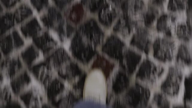 Solo walk on damp streets, Lone pedestrian cautiously crossing wet cobblestones in darkness, Quiet person wandering alone through illuminated evening streets and ancient plaza under night sky