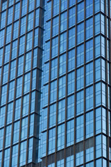 Obraz premium Modern glass skyscraper facade with repeating geometric patterns and blue reflections