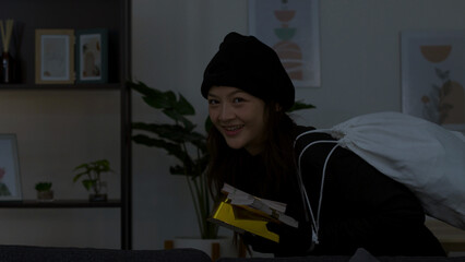Asian Female Burglar in Black Beanie Stealing Cash in Living Room © blueringmedia