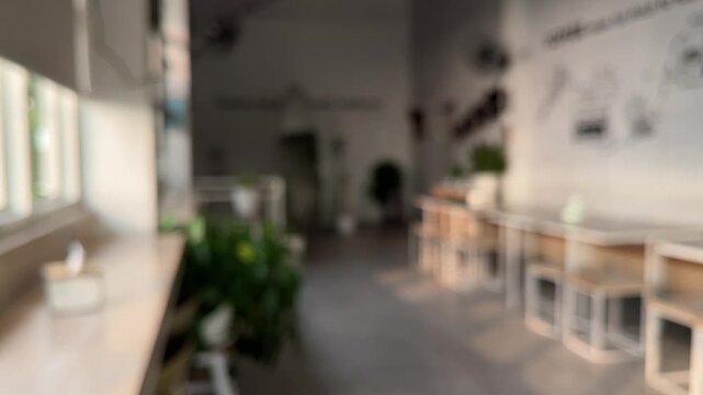 blurred of interior cafe, coffee shop, restaurant. empty wooden tables And chairs, indoor seating. Plants, leaves, green, nature, white wall, lamps. windows. bright. dark, shadows. blurry, blur, 