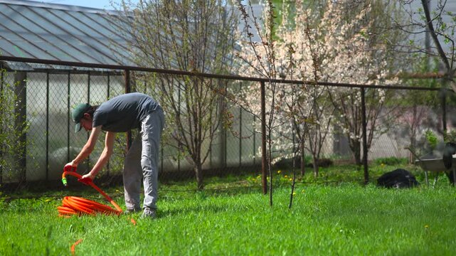 Man bending over orange bucket in sunny backyard garden