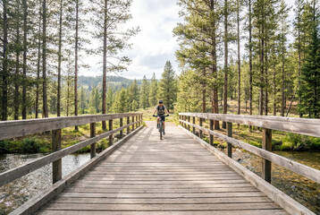 Fototapeta premium Female eMTB Rider Crossing Bridge on Forest Singletrack