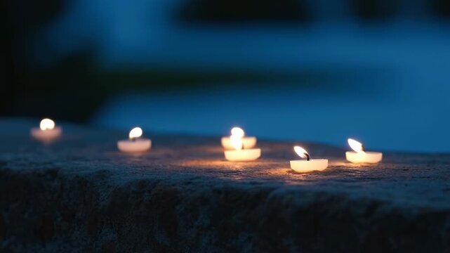 Row of tea light candles glowing on rough stone at dusk