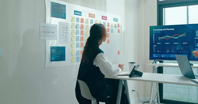 Group of Asian businesspeople work together leads business meeting uses presentation TV with revenue, profit or sale statistics in office. Financial generation z team brainstorm on e-Commerce project.