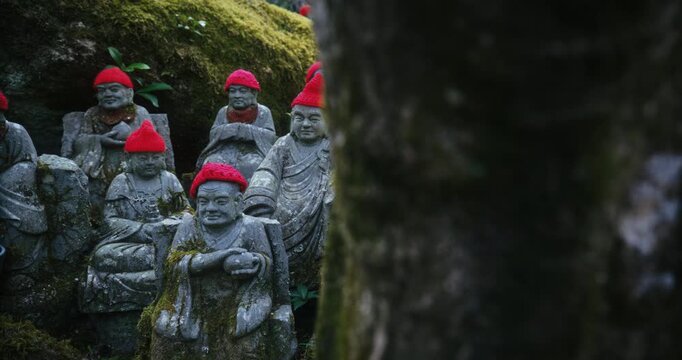 Small Stone Rakan Statues with Red Knit Hats on Moss-Covered Rocks Japan - steady cam movement