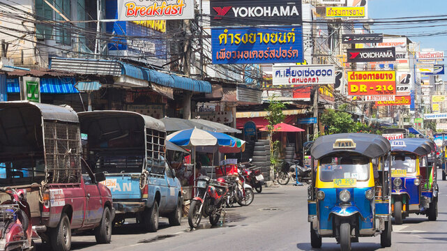Tuk tuks driving past car tyre shops, Bangkok, Thailand